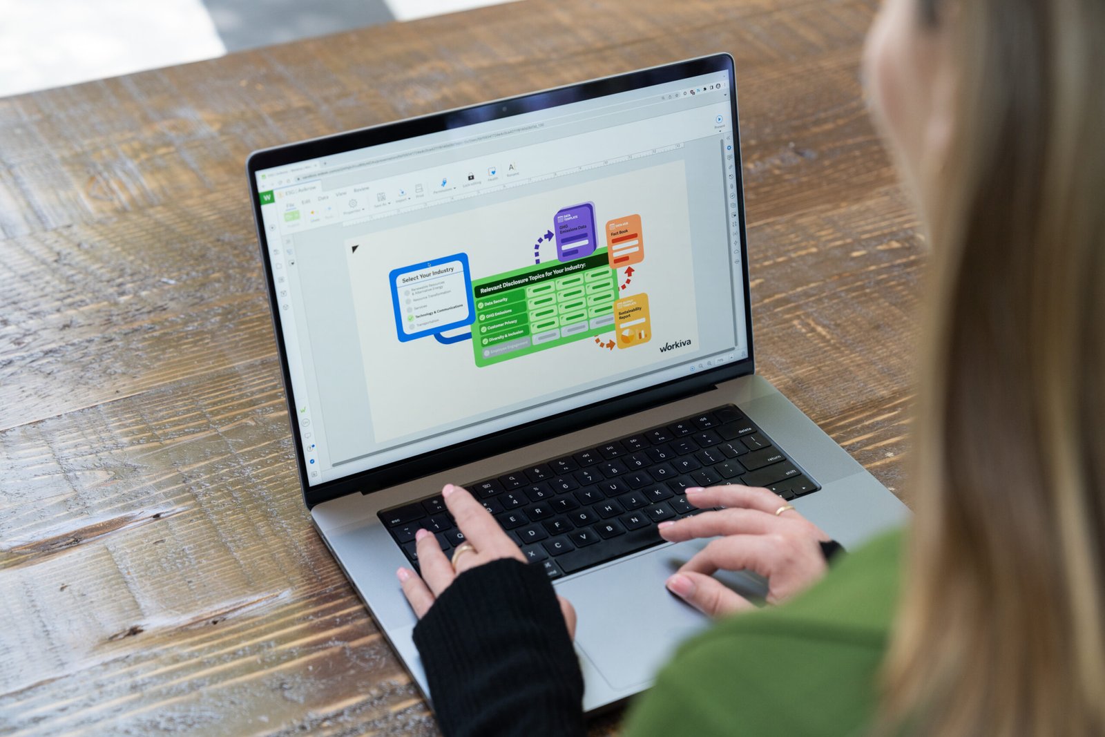 Person using a laptop displaying Workiva's ESG disclosure workflow on a wooden table.
